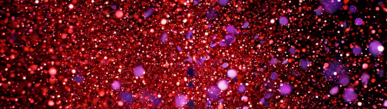 Celebration and festive energy red and purple glitter explosion on black background slow motion burst of sparkling particles for holiday event and party backdrop.