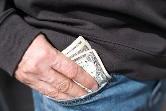 A man puts US dollars into the pocket of his jeans.
