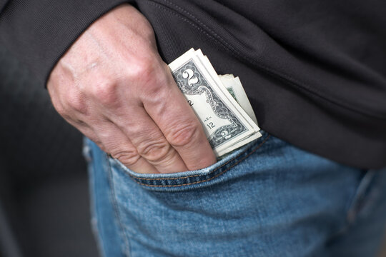 A man puts US dollars into the pocket of his jeans.
