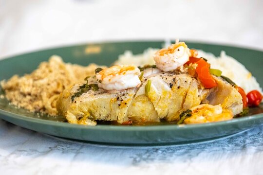 Moqueca capixaba, traditional Brazilian seafood stew with snook fish, shrimp, tomato and coriander, served on a green plate with white rice and farofa.