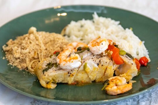 Moqueca capixaba, traditional Brazilian seafood stew with snook fish, shrimp, tomato and coriander, served on a green plate with white rice and farofa.
