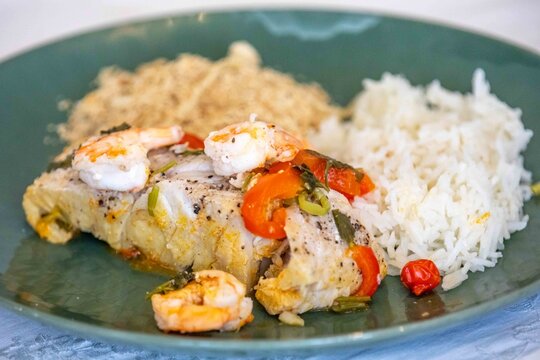 Moqueca capixaba, traditional Brazilian seafood stew with snook fish, shrimp, tomato and coriander, served on a green plate with white rice and farofa.