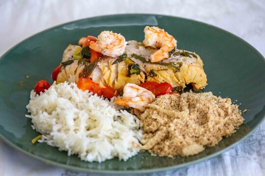 Moqueca capixaba, traditional Brazilian seafood stew with snook fish, shrimp, tomato and coriander, served on a green plate with white rice and farofa.