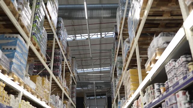 Wholesale supermarket aisle with tall industrial shelves loaded with bulk foods and drinks supplies on wooden pallets showing warehouse retail inventory and storage stock