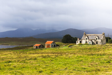 Abandoned stone cottage and rusted farm buildings on remote Scottish highland croft under dramatic stormy sky, Scotland, United Kingdom © EyesTravelling