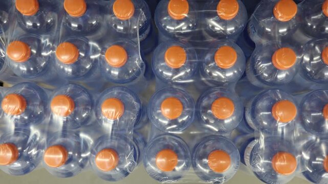 Plastic water bottles with orange caps are tightly packed in shrink wrap for retail sale showing bottled drinking water in bulk packaging for everyday household daily use
