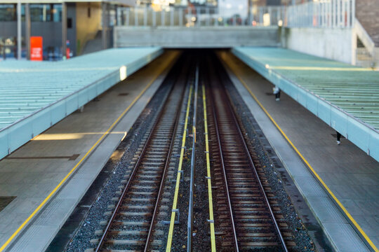 Train tracks and empty platforms converging at the entrance of a dark underground tunnel, representing urban transit, journey, and transportation infrastructure