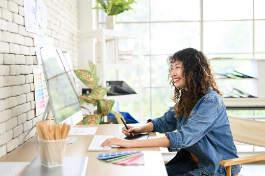 Asian female artist drawing something on graphic tablet. graphic designer working at office.