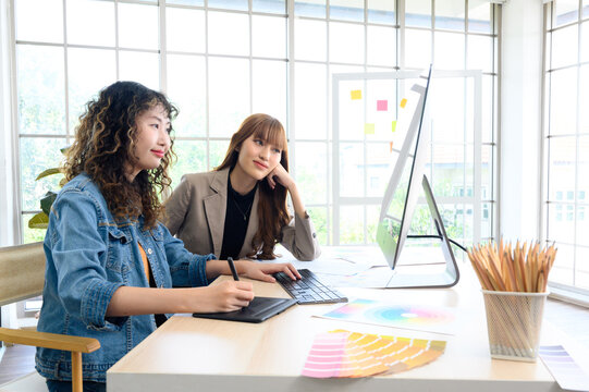 Happy two young female graphic designers discussing with colleague in office. Creative people working together using computer at desk.