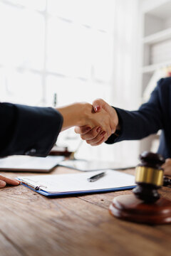 Handshaking business people making a legal agreement after signing a contract, finalizing partnership details in a professional office setting with a gavel on the table