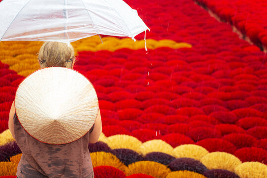 A woman in a conical hat with an umbrella among multi-colored incense sticks. Quang Phu Cau, Hanoi, Vietnam.