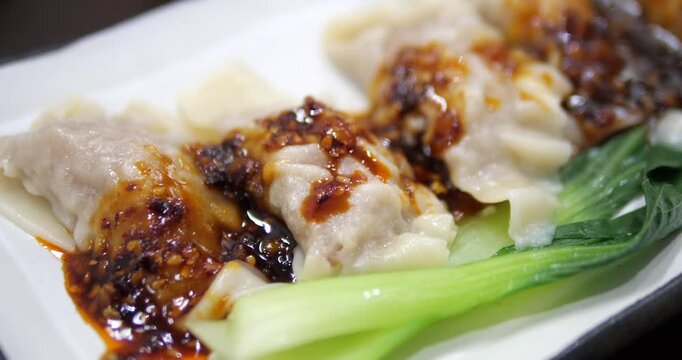 Close up of spicy Chinese wontons in chili oil with bok choy on white plate