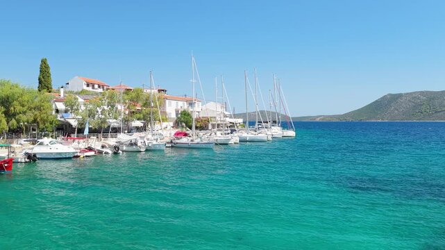 A harbor scene in Steni Vala, Alonnisos, Greece, featuring several sailboats and yachts moored along the waterfront