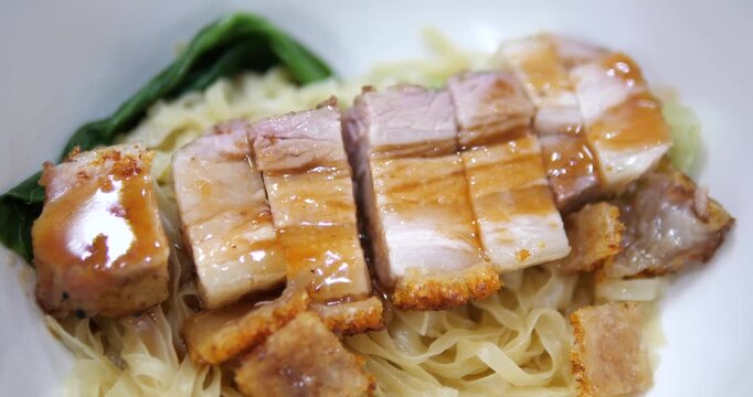 Close up of crispy pork belly over flat egg noodles on bowl
