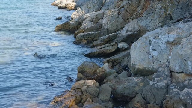 Rocky coastline at Steni Vala on Alonnisos island, Greece. Rugged stone formations meeting the clear blue Aegean Sea, with gentle waves lapping against the rocks