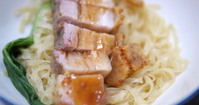 Close up of crispy pork belly over flat egg noodles on bowl