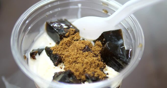 Close up of black grass jelly with fresh milk topped with brown sugar in plastic cup