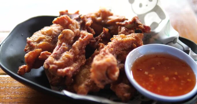 Close up of crispy deep fried chicken tendons with sweet chili sauce on black plate