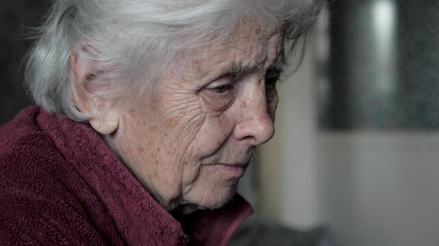 Close up profile pensive senior woman with deep wrinkles and gray hair, looking down with thoughtful and melancholic expression, reflecting on life and memories at home. Elderly people in nursing home