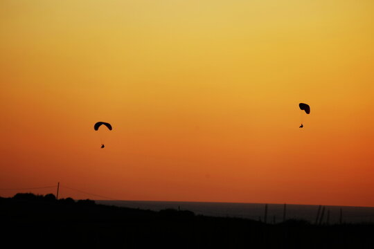 Silhouettes of Paragliders Flying Against Vibrant Orange Sunset Sky over Coastal Horizon