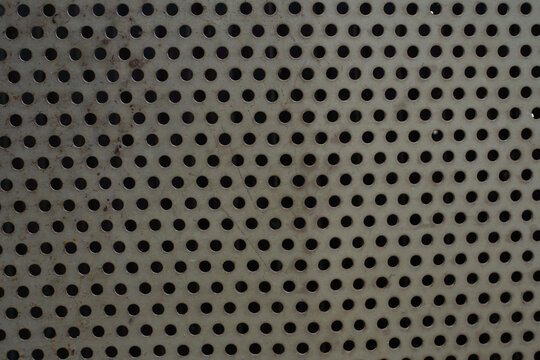 Close-up of a perforated metal sheet with a regular pattern of round holes, creating an industrial textured background