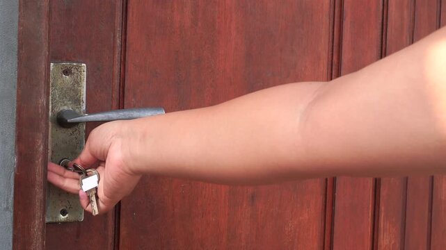 Close up of a person unlocking and opening a wooden door with key.