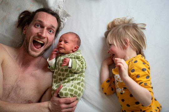 A dad with his two baby girls lying on a bed
