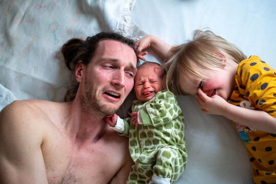 A dad with his two baby girls lying on a bed