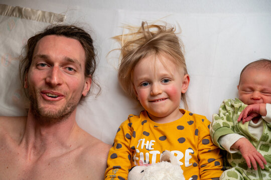 A dad with his two baby girls lying on a bed