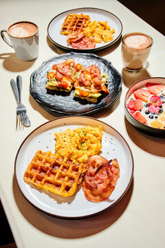 Delicious breakfast spread with waffles, bacon, eggs, and chocolate