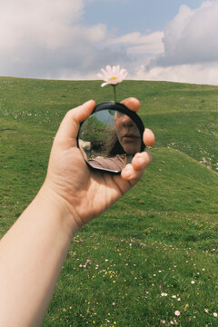 Person holding a mirror with flower in hand on green hill