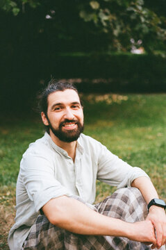 Man Sits on Grass and Smiles During Sunny Day in Park