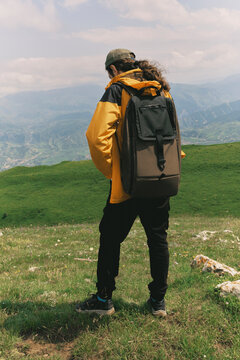 Hiker stands on green hill with backpack and mountains behind