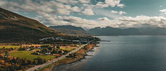 Vertical aerial view of a scenic coastal road winding past a village and mountains along the ocean in northern Norway with copy space in sky © Quality by Simon