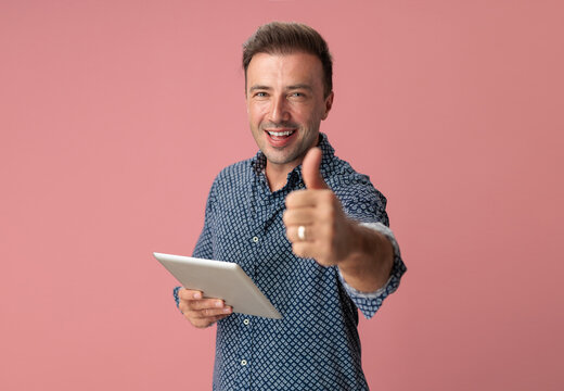 Enthusiastic man showing thumbs up while holding digital tablet