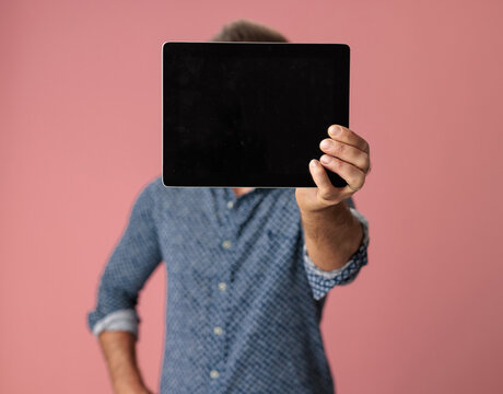 Casual man holding blank digital tablet covering face
