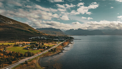 Vertical aerial view of a scenic coastal road winding past a village and mountains along the ocean in northern Norway with copy space in sky © Quality by Simon