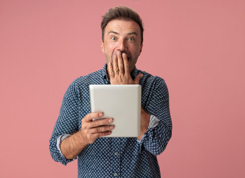 Shocked man covering mouth while holding digital tablet