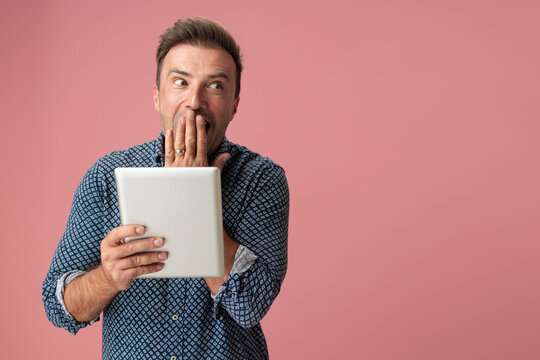 Stunned man holding digital tablet and covering mouth