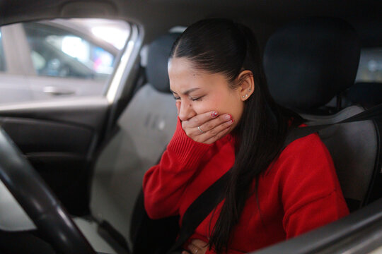 Sick young woman covering her mouth in car
