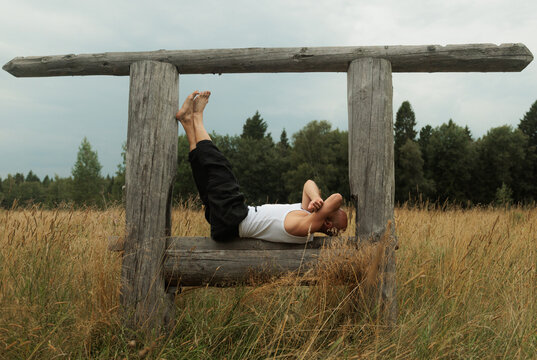 Person Resting on a Wooden Structure in a Field During a Cloudy Day