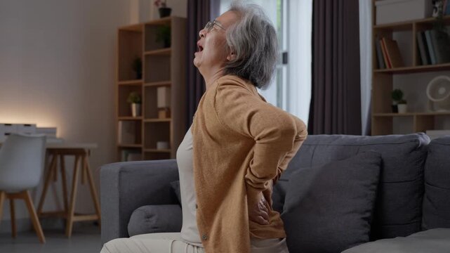 Elderly female patient stretching sore back suffering from muscle stiffness indoors