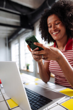 Smiling Woman Using Smartphone While Working On Laptop