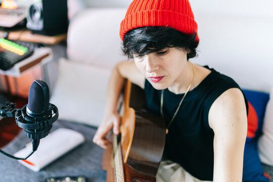 Woman playing acoustic guitar recording music at home studio