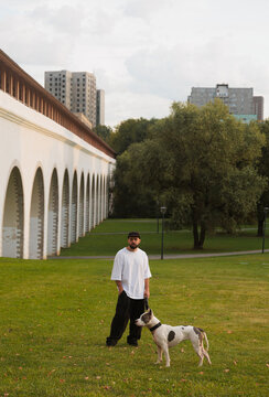 Man Walking With Dog in City Park Near Historirc Building With Arches