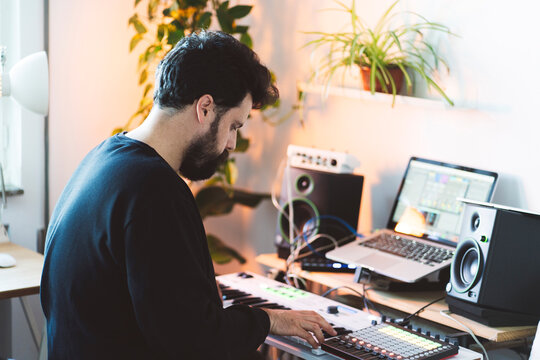 Man creating music in home studio with synthesizer and laptop