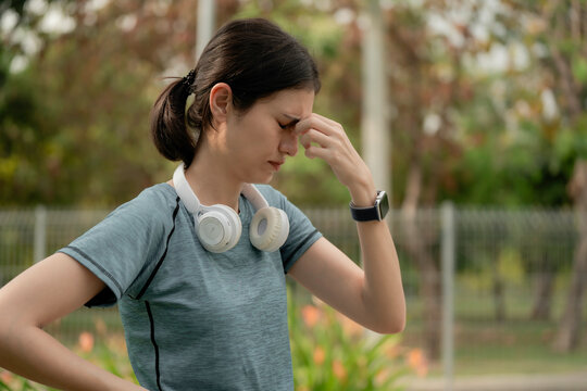 Young woman feeling dizzy and stressed during outdoor workout in park, wearing headphones and smartwatch, fatigue, headache, overtraining and health risk concept, woman, dizzy, stress, headache,