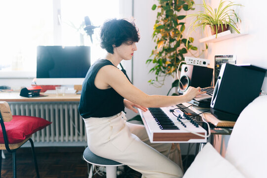 Woman producing music using a synthesizer and laptop in home studio