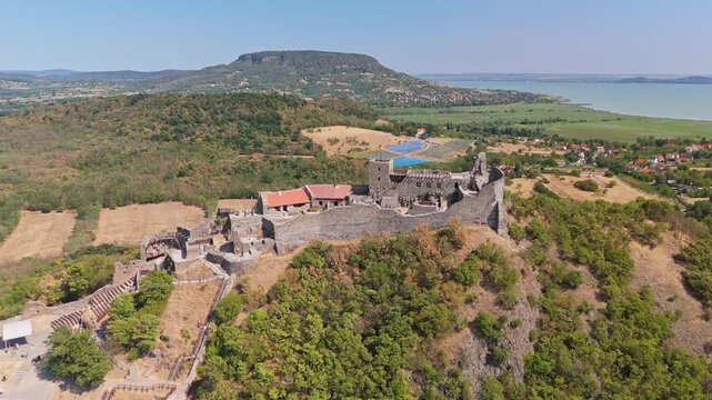 Szigliget Castle ruins overlooking Lake Balaton in Veszpr&eacute;m County, Hungary, with medieval stone walls, towers, village, forest and countryside landscape, filmed by drone.