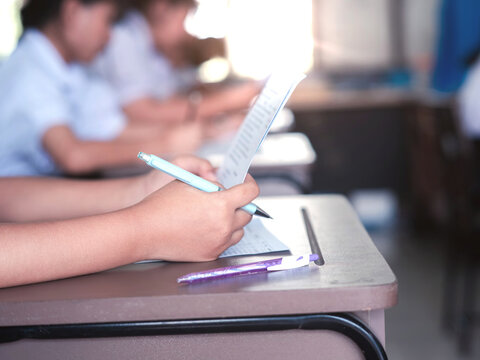 Students reading exam answer sheets exercises in classroom of school with headache and stress